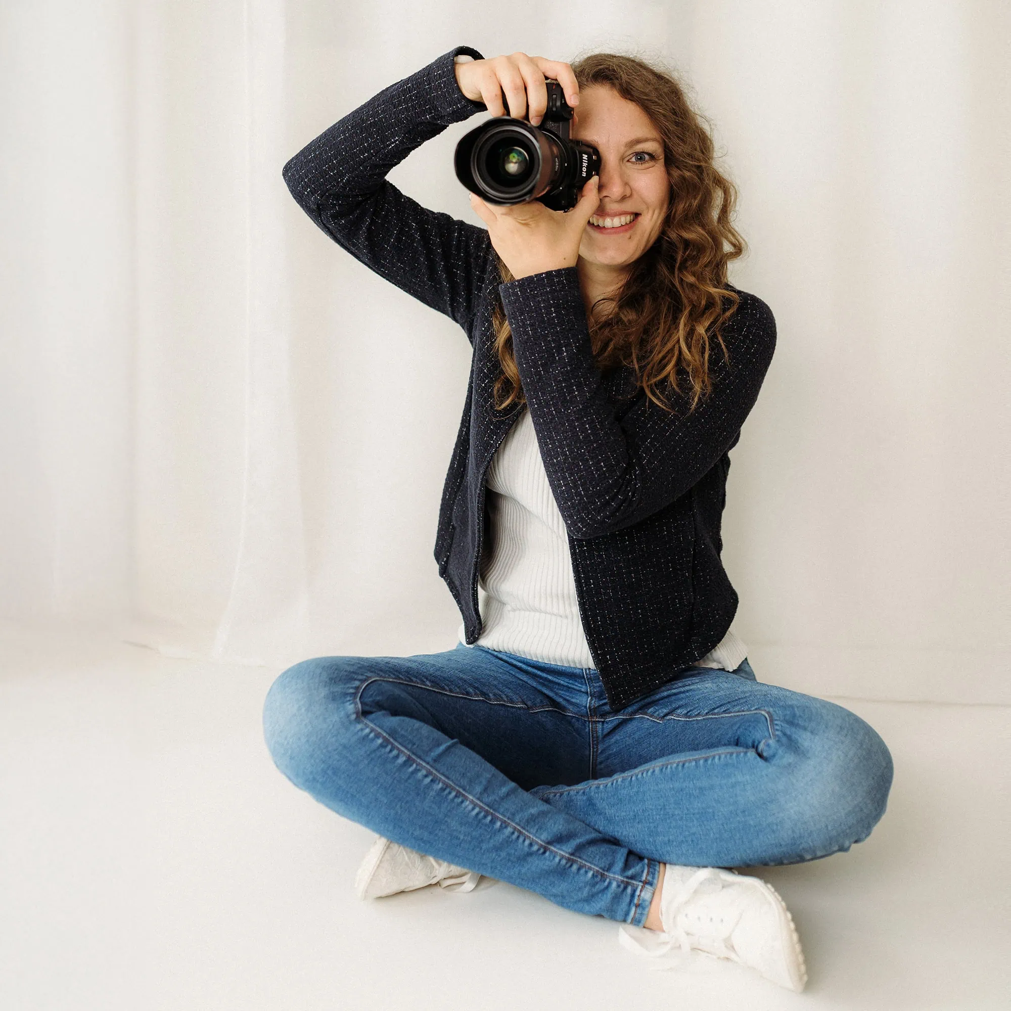 Die Businessfotografin Mica Zeitz, Fotografenmeisterin aus Ingolstadt, präsentiert sich in diesem Bild kreativ und einladend. Mit ihrer professionellen Kamera fängt sie nicht nur Momente ein, sondern verkörpert auch ihre Leidenschaft für die Fotografie in einem modernen Setting.